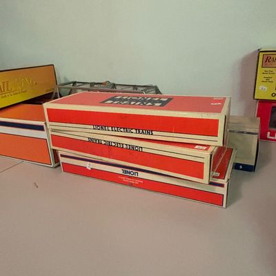 Stack of vintage Lionel Electric Trains boxes, showing some wear consistent with age, alongside other model train packaging on a table.