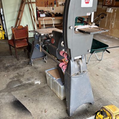 Vintage Shopsmith multi-purpose woodworking tool system, including a bandsaw attachment, shown in a garage setting with other tools.