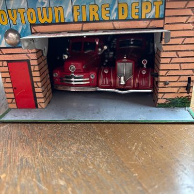 Vintage Marx Toytown Fire Dept. lithographed tin toy garage with two red fire trucks, showing some wear consistent with age.