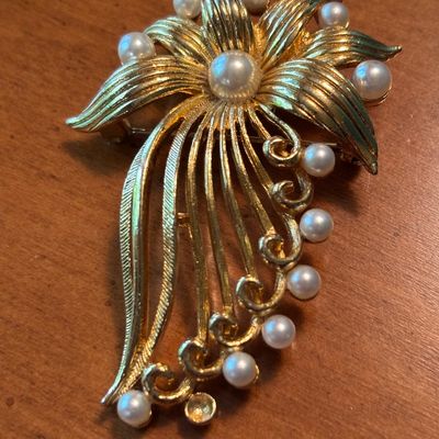 Vintage gold-tone floral brooch featuring textured petals and faux pearl accents, with one missing pearl at the bottom.