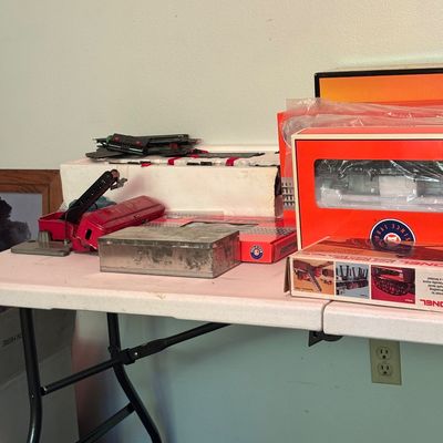 Assorted vintage Lionel model train accessories and track pieces, some in original boxes, displayed on a white folding table.