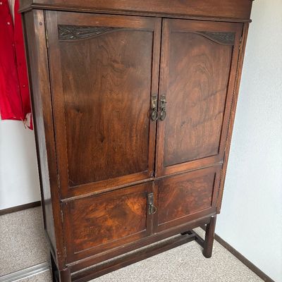 Antique wooden armoire featuring a broken pediment top, carved details on the upper doors, and burl wood veneer panels on the lower...