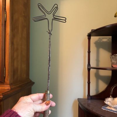 Vintage wire rug beater with a star-shaped head and a turned wooden handle, showing signs of age and use.