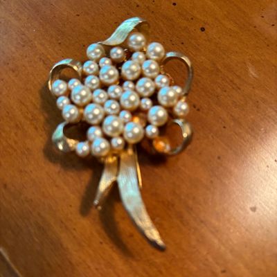 Vintage gold-tone brooch featuring a cluster of faux pearls in a floral or bouquet design with textured ribbon details.