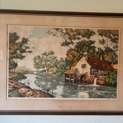 Framed landscape print depicting a rustic watermill beside a river, signed by the artist in the lower right corner.