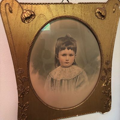 Antique hand-colored portrait of a young girl in an ornate Art Nouveau gold-painted frame with raised floral motifs.