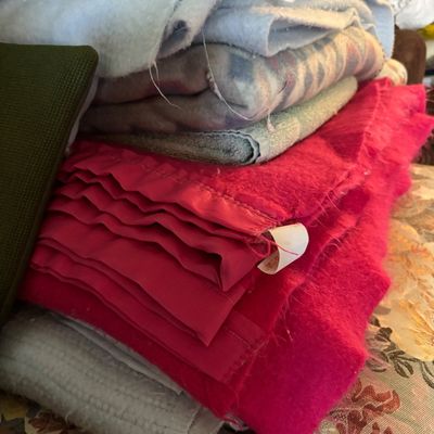 Stack of vintage blankets and textiles, including a vibrant pink wool blanket with satin binding and various patterned and solid-colored...