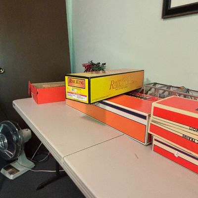 MTH RailKing and Lionel model train boxes displayed on a folding table, showing some wear to the packaging.