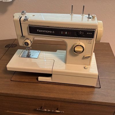 Vintage Kenmore 6 sewing machine in a wooden cabinet, featuring a cream-colored body with stitch selection dials.