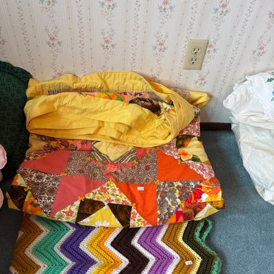 Vintage handmade patchwork quilt with vibrant orange, yellow, and floral patterns, paired with a colorful crochet chevron afghan blanket.