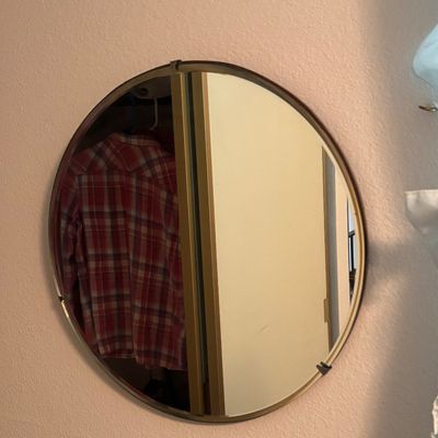 Mid-century modern round wall mirror with a thin brass frame and mounting clips, reflecting a closet interior.