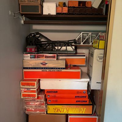 Collection of vintage Lionel and RailKing model train sets, track, and accessories, mostly in original boxes, stored on closet shelves.