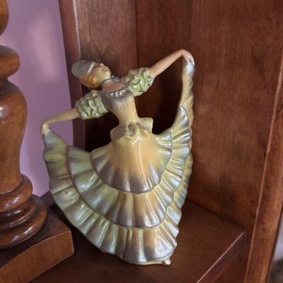 Vintage ceramic figurine of a Spanish dancer in a ruffled yellow and silver dress, displayed on a wooden shelf.