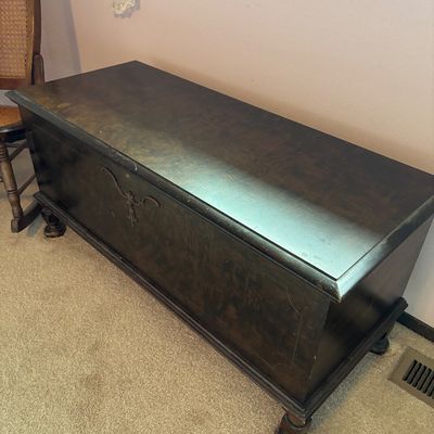 Vintage dark-stained wooden hope chest featuring a decorative metal escutcheon on the front and turned wooden feet.