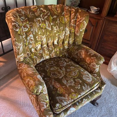 Vintage channel-back wing chair upholstered in a 1970s floral pattern of olive green, gold, and cream, featuring carved wooden cabriole...
