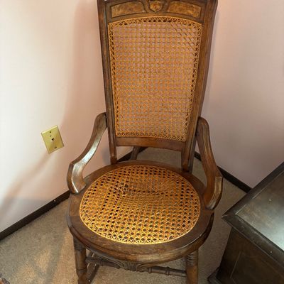 Antique wooden rocking chair featuring a woven cane seat and backrest, with carved details on the top rail and curved armrests.