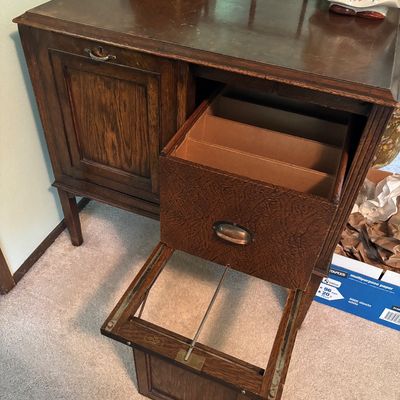 Antique oak sheet music cabinet featuring a drop-front door and a pull-out drawer with vertical dividers, showing some surface wear...