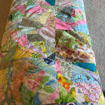 Vintage handmade crazy quilt featuring a colorful patchwork of floral, paisley, and geometric patterned fabrics, tied with green yarn.