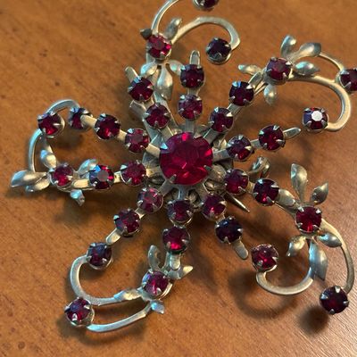 Vintage silver-tone starburst brooch featuring prong-set ruby red rhinestones and delicate leaf accents, circa mid-20th century.