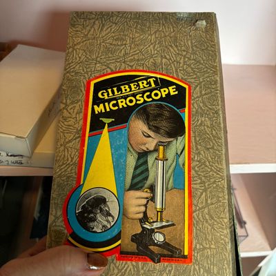 Vintage Gilbert Microscope set in its original textured cardboard box, featuring mid-century graphic illustration on the cover.