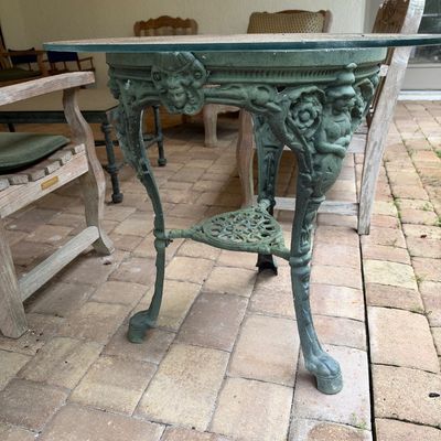 Sale Photo Thumbnail #143: Ornate cast iron patio table with a green verdigris finish, featuring a glass top, figural leg details