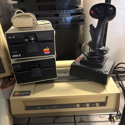 Vintage Apple computer peripherals, including two Disk II floppy drives, an Apple dot matrix printer, and a CH Products flight stick...