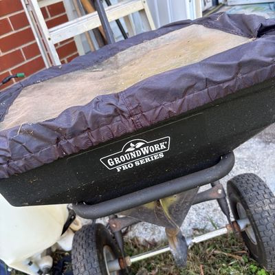 GroundWork Pro Series walk-behind broadcast spreader with a black hopper and protective fabric cover, showing light outdoor wear.