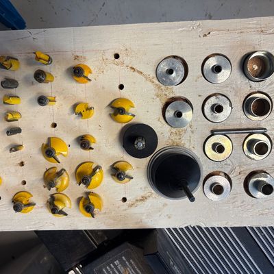 Assorted router bits with 1/4-inch shanks and various metal collets, organized on a custom wooden holder.