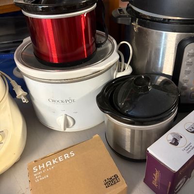 Assorted kitchen appliances including a classic white Crock-Pot slow cooker, a small red dipper crock, a stainless steel mini slow...