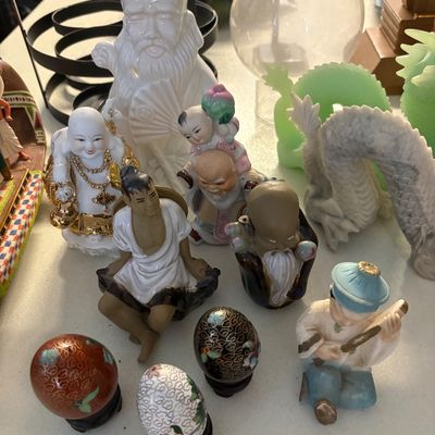 Collection of Asian-themed decorative figurines and cloisonné eggs, including a white porcelain Shou Lao figure, a laughing Buddha, and a...