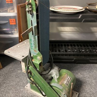 Vintage green benchtop belt sander with a mounted electric motor and a blue sanding belt.