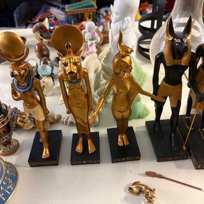 Collection of Egyptian-themed figurines, including gold and black statues of deities like Anubis, Horus, and Sekhmet, displayed alongside...