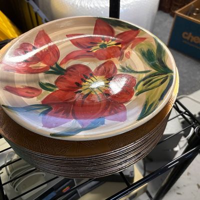 Stack of vintage hand-painted ceramic plates featuring a vibrant red floral design, resting on a wire shelf.