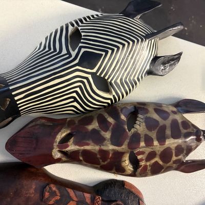 Two hand-carved African-style wooden masks depicting a zebra and a giraffe, featuring painted details and cut-out eyes.