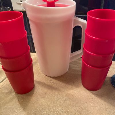 Sale Photo Thumbnail #174: Vintage white Tupperware pitcher with a red push-button lid, flanked by two stacks of matching red plastic cups.