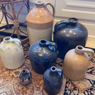 Sale Photo Thumbnail #133: Collection of antique and vintage stoneware jugs in various sizes, glazes, and colors resting on a patterned rug.