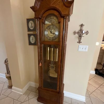 Sale Photo Thumbnail #11: Traditional oak Ridgeway grandfather clock featuring a bonnet top, ornate brass clock face with moon phase dial, visible brass chimes, and a decorative pendulum inside a glass display case.