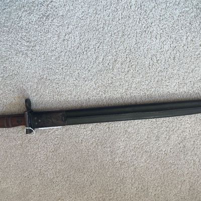 Sale Photo Thumbnail #57: Vintage military bayonet with a wood handle and matching dark metal scabbard.