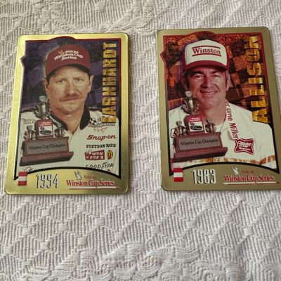 Sale Photo Thumbnail #42: Pair of metallic NASCAR Winston Cup Series commemorative trading cards featuring Dale Earnhardt (1994) and Bobby Allison (1983). Both cards display bold portraits and trophy imagery in good condition.