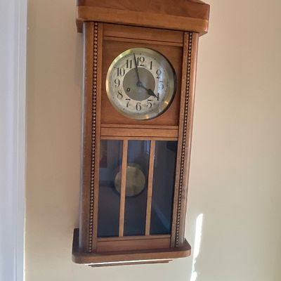 Sale Photo Thumbnail #87: Vintage wooden wall clock with a brass-toned dial, pendulum display case, and arched top crest.