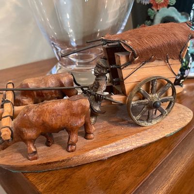 Sale Photo Thumbnail #49: Miniature vintage hand-carved wooden ox cart figurine, featuring fur canopy detailing and metal wheels mounted on an oval base.