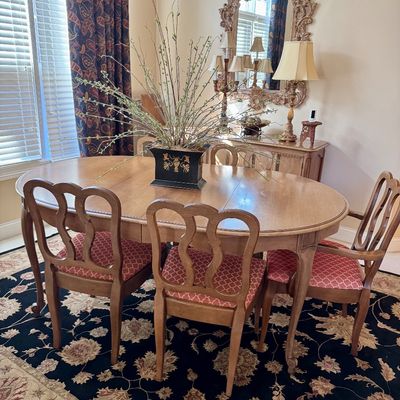 Sale Photo Thumbnail #2: Traditional wooden extension dining table set with French-style dining chairs upholstered in pink patterned fabric, accompanied by a matching buffet, elaborate carved mirror, and large floral centerpiece.
