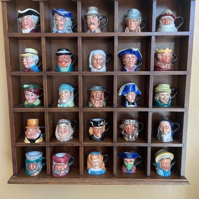 Sale Photo Thumbnail #54: Collection of 25 miniature Royal Doulton character jugs displayed in a wooden shadow box rack.
