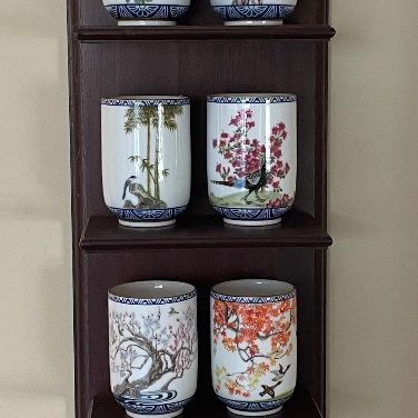 Sale Photo Thumbnail #58: Set of 12 Asian-style porcelain tea cups featuring nature and floral motifs, displayed on a tiered dark wood hanging shelf.