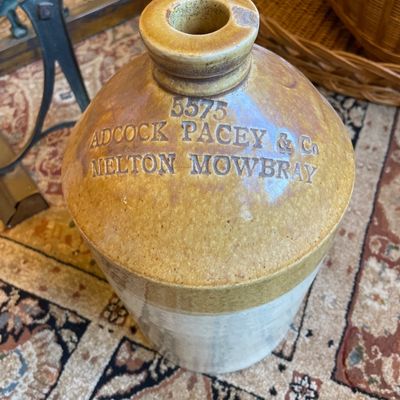 Sale Photo Thumbnail #125: Antique stoneware whiskey or spirit jug impressed with 'Adcock Pacey & Co Melton Mowbray 5575', featuring a two-tone glaze and top loop handle.