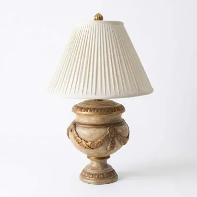 Sale Photo Thumbnail #33: Neoclassical urn-style table lamp featuring a distressed beige and gold finish with relief-carved swags, topped with a pleated white fabric shade.