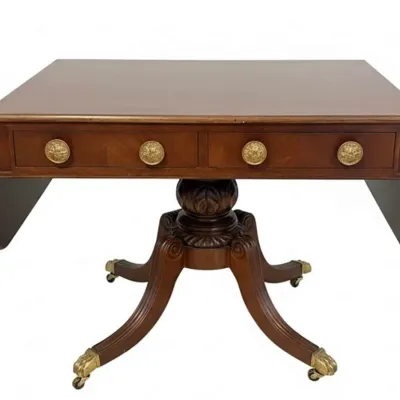 Sale Photo Thumbnail #58: Duncan Phyfe style mahogany drop-leaf table featuring a single drawer with ornate brass pulls, supported by a carved pedestal base on four splayed legs with brass paw casters.