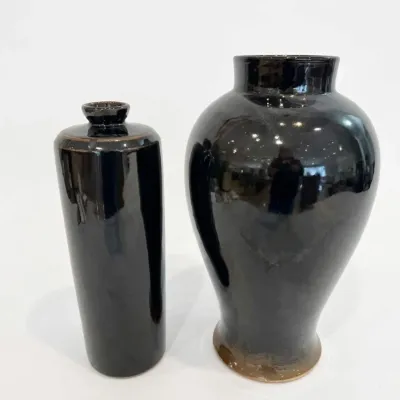 Sale Photo Thumbnail #56: Two contemporary ceramic vases with a glossy black glaze, featuring a tall cylindrical bottle vase and a larger baluster-shaped vase.