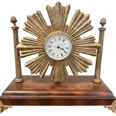 Sale Photo Thumbnail #46: Neoclassical style mantel clock featuring a gilt sunburst dial flanked by fluted columns, mounted on a polished wood base with ornate brass feet.