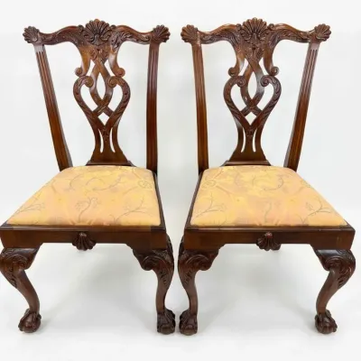 Sale Photo Thumbnail #18: Pair of Chippendale-style mahogany side chairs featuring ornate carved splats, shell motifs, cabriole legs, and claw-and-ball feet, upholstered in a patterned yellow fabric.